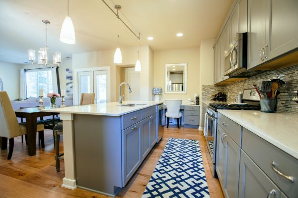 Modern home kitchen diner with green grey fitted units, a kitchen island and blue floor rug.